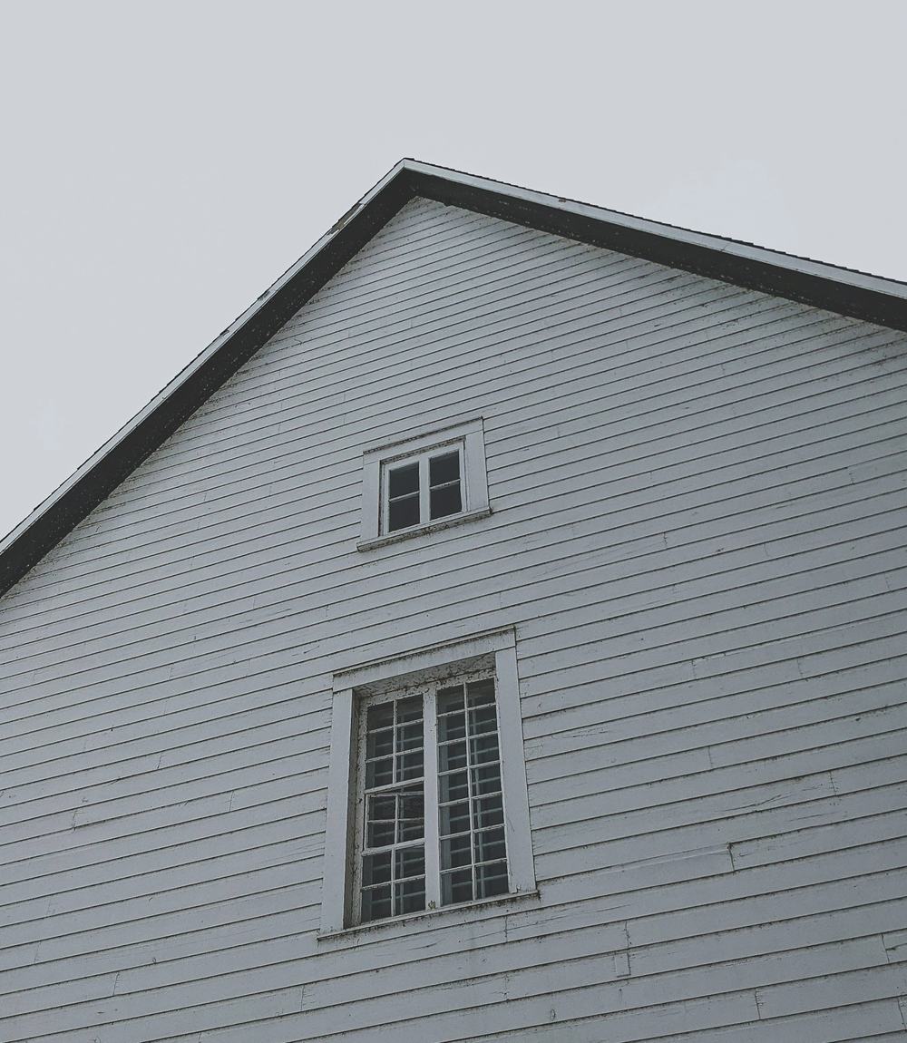 A pale grey clapboard gable end with three white sash windows