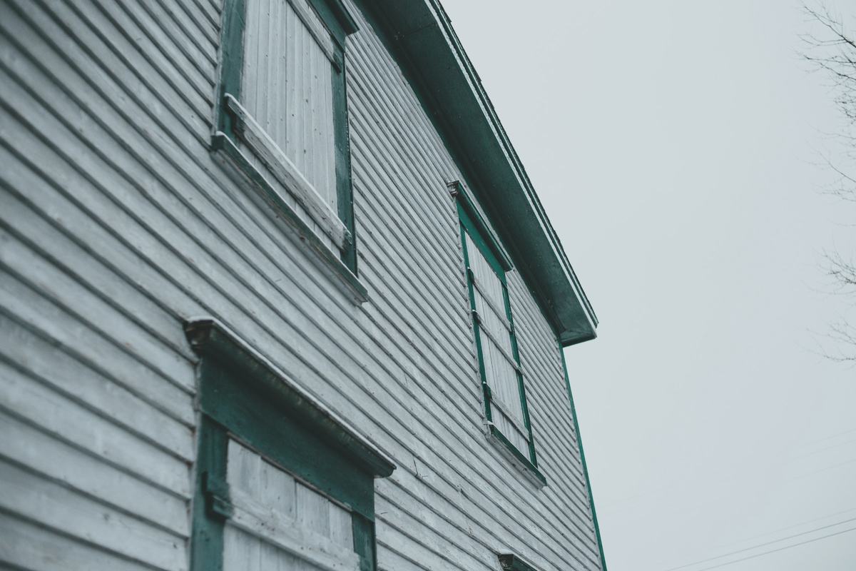 Weathered clapboard siding with dark green window trim against an overcast sky