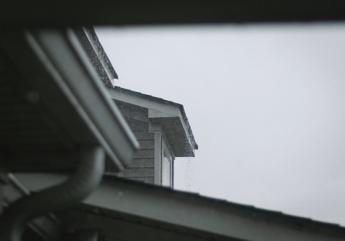 A white seamless gutter and downspout under a grey sky